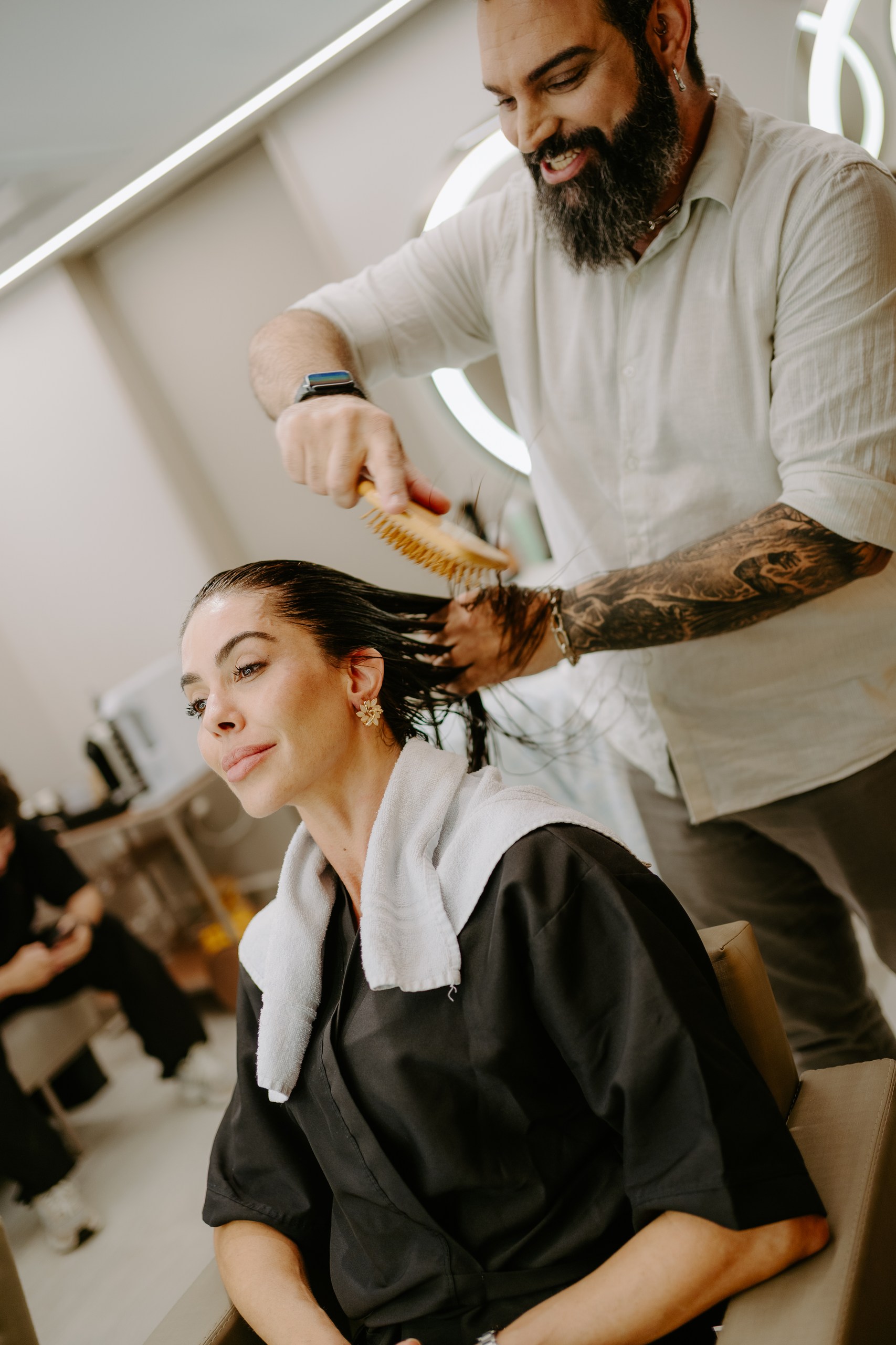 Felipe Messias sorri enquanto escova os cabelos de uma cliente no DOM Hair