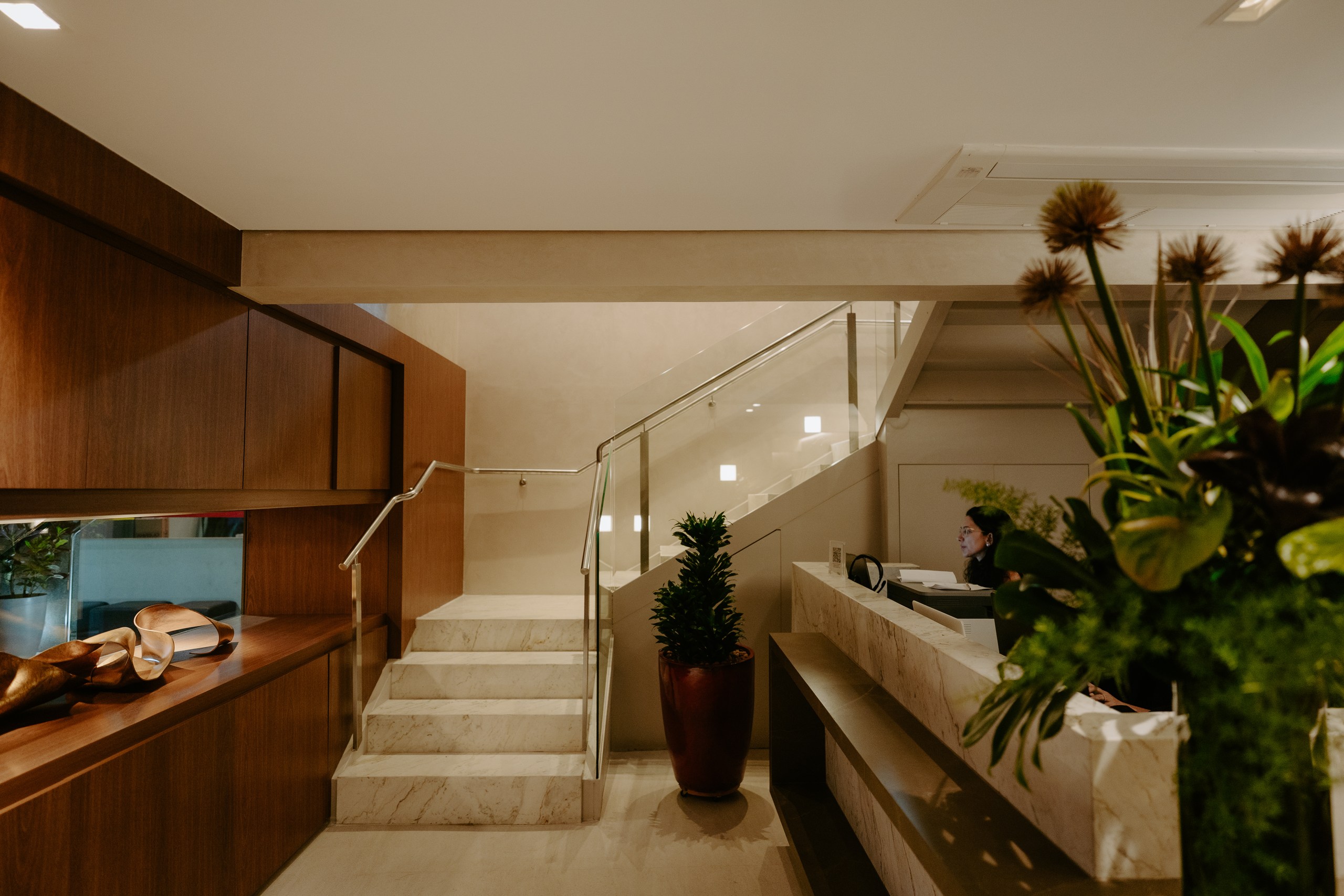Lobby da clínica com escada de mármore, plantas e balcão de recepção