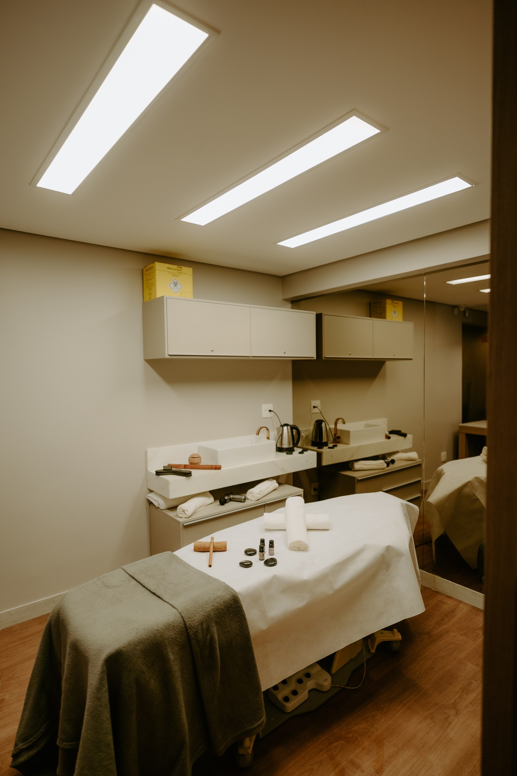 Sala de terapias com maca preparada, toalhas, pedras e óleos essenciais