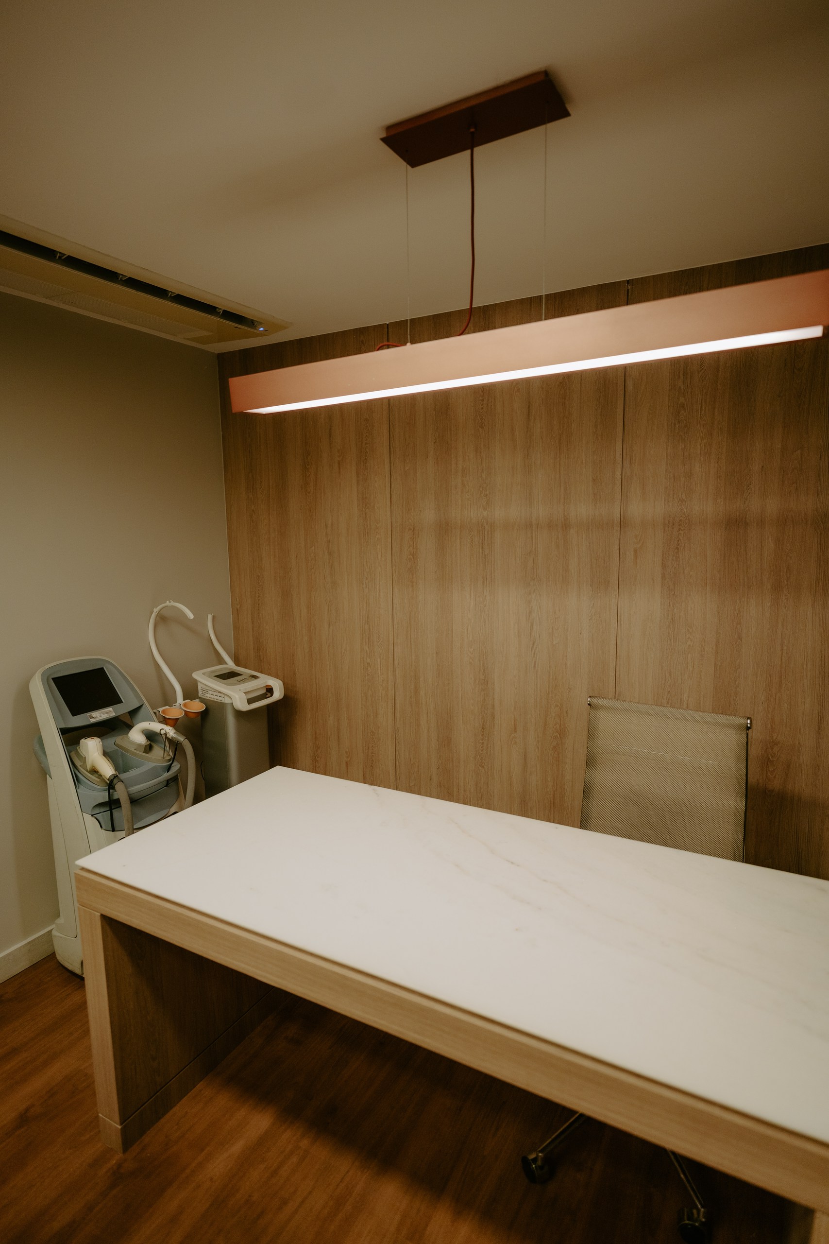 Sala de procedimentos com maca de superfície clara e equipamentos de tecnologia estética