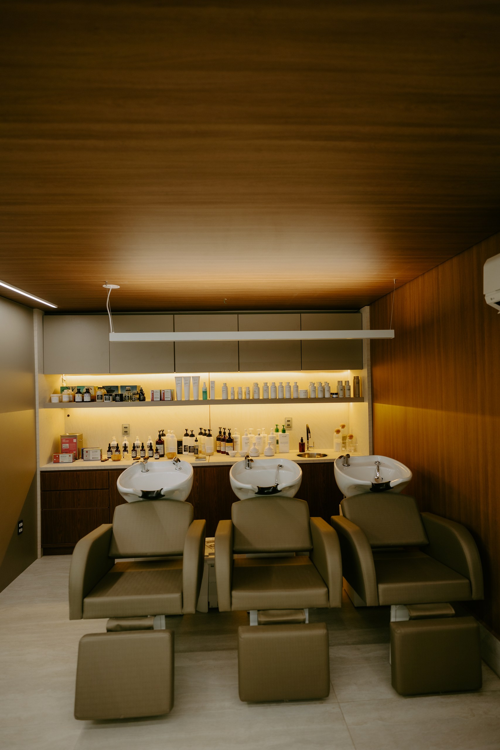 Sala de lavagem do DOM Hair com três lavatórios e prateleiras de produtos iluminadas