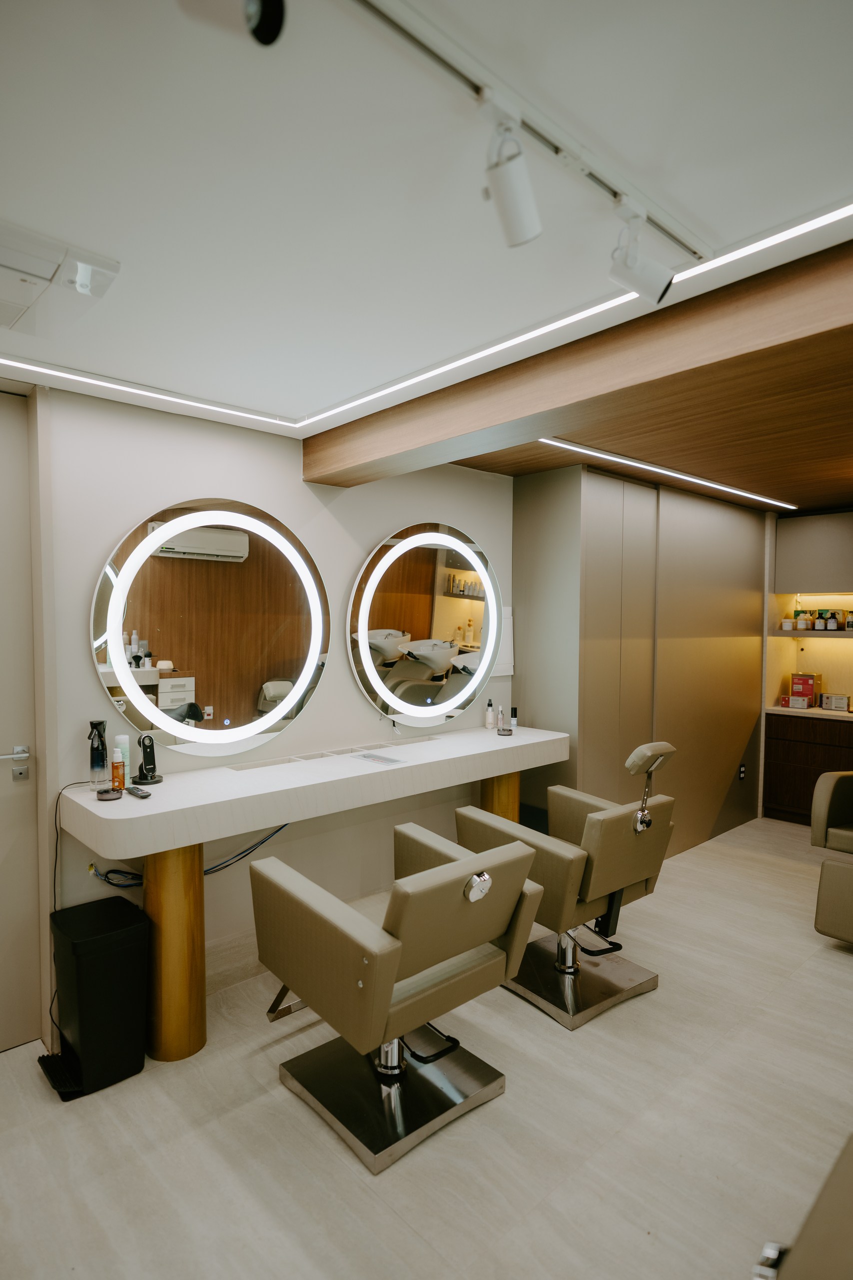 Bancada do DOM Hair com espelhos redondos iluminados e cadeiras de atendimento